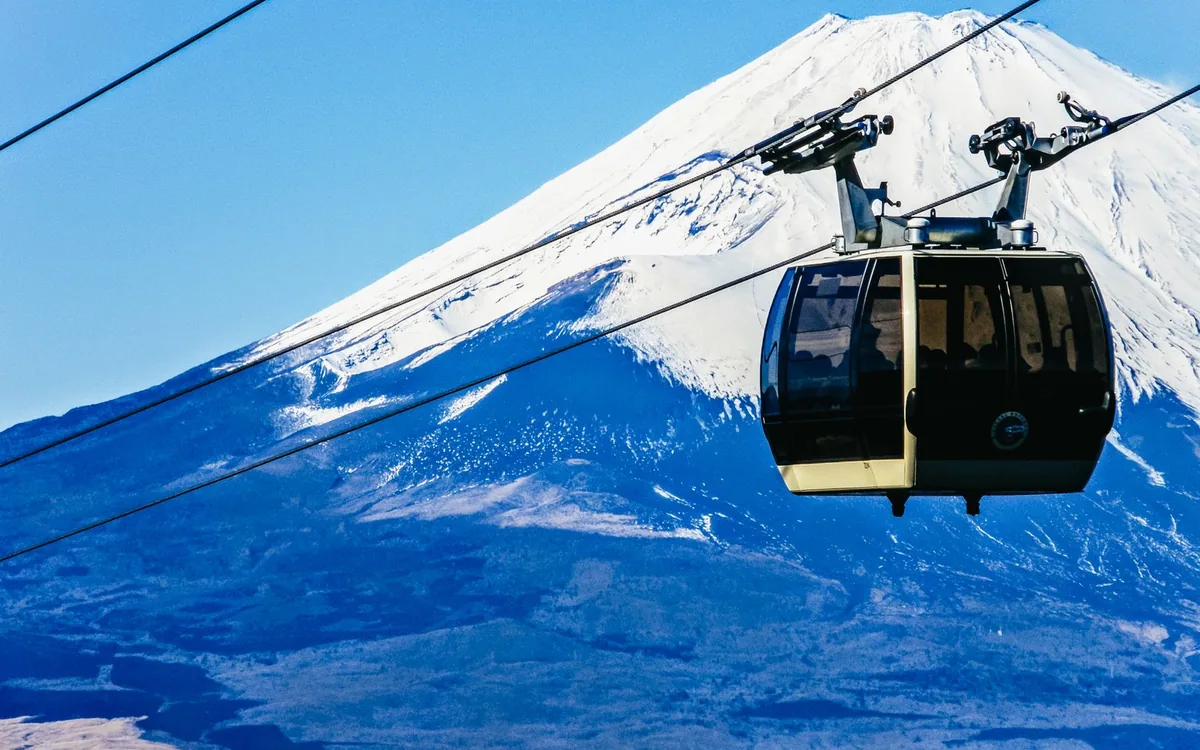 A ropeway cabin hanging above the snow line with Mount Fuji behind it