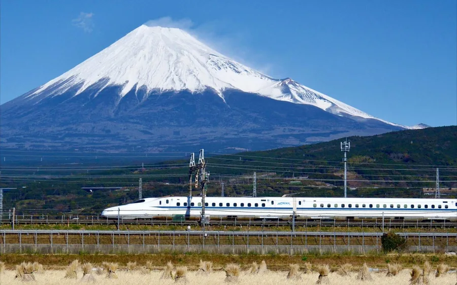 A shinkansen running past open fields with Mount Fuji behind