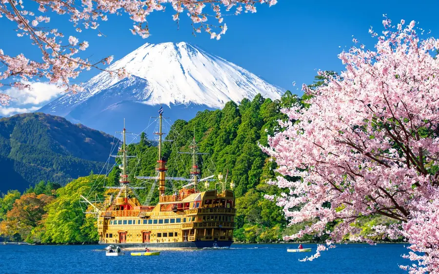 A sightseeing ship on Lake Ashi with cherry blossom and Mount Fuji behind